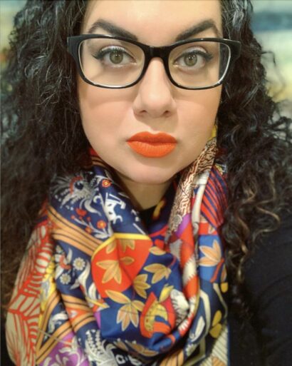 Headshot of Andrea wearing dark-rimmed glasses and bright lipstick